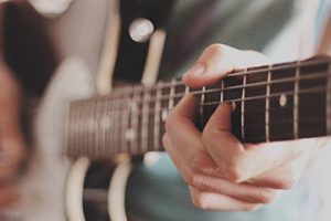 Image of a guitar with two hands playing it