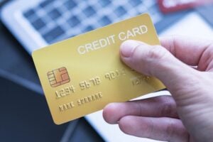 Photo of a person holding a credit card by a laptop