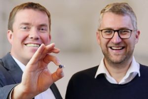 Photo of two men, one holding a small hearing aid