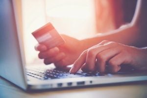 A person holding a credit card over a laptop keyboard