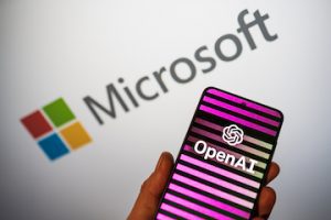 OpenAI logo on phone in a hand and blurred Microsoft