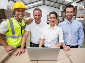 Warehouse managers and worker smiling at camera in a large warehouse